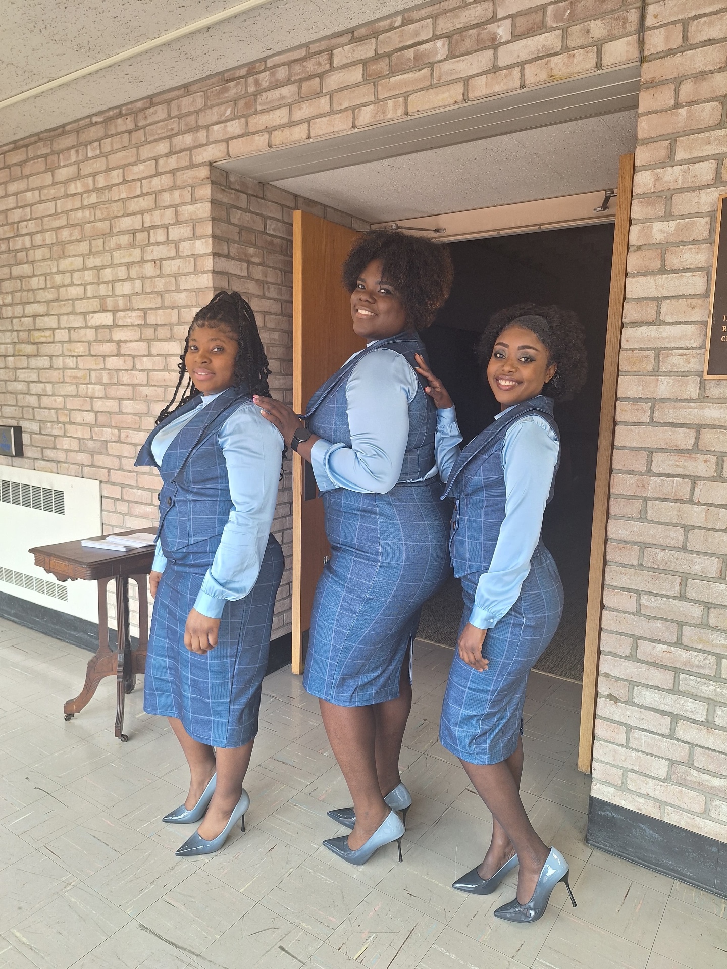 Three MAS-B singers in blue plaid ministry attire standing in profile at a church entrance