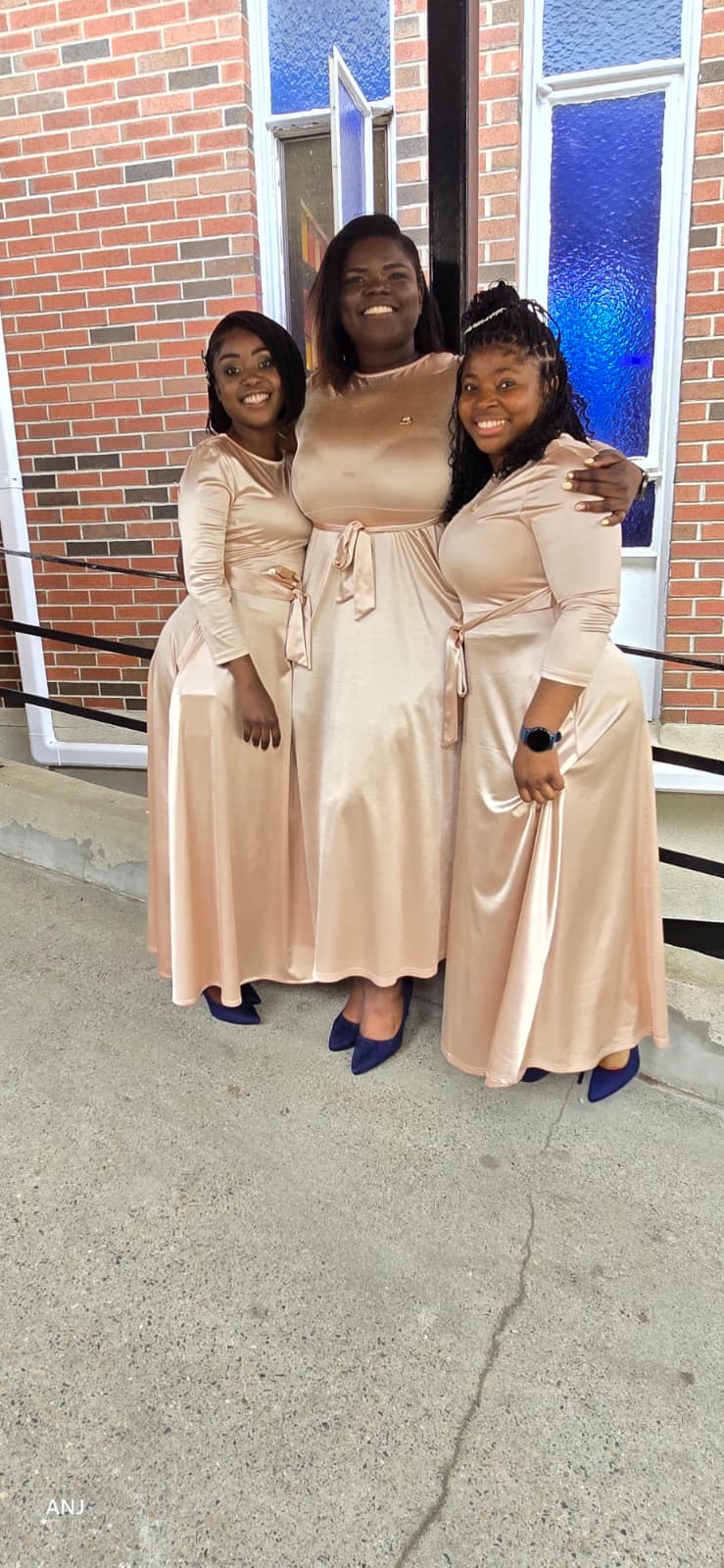 Three MAS-B Vocal Ministry members embracing in champagne gowns at the chapel entrance