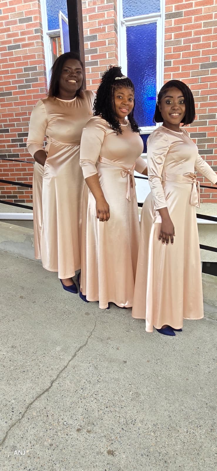 Three MAS-B singers in champagne satin gowns smiling outside a church entrance